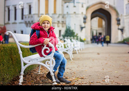 Niedliche schönes Kind, junge, sitzen auf einer Bank vor wunderschönen Renaissance-Schloss Hluboka in der Tschechischen Republik Stockfoto