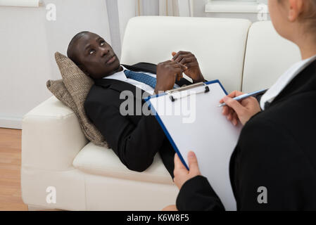 Weibliche Psychiater Notizen In der Vorderseite des Patienten während der psychologischen Therapie Sitzung Stockfoto