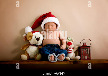 Neugeborenes Baby Boy das Tragen einer Mütze und Jeans, schlafen auf einem Regal neben Teddybären. Im Studio auf einem cremigen Hintergrund Geschossen, geschossen von abov Stockfoto