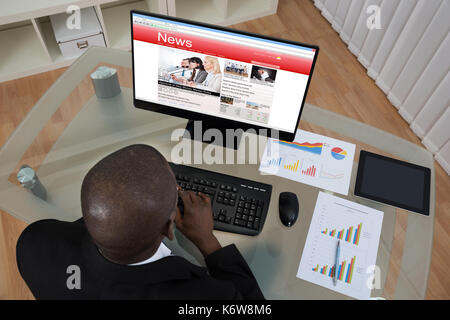 Junge afrikanische Unternehmer auf der Suche nach Business Nachrichten auf Computer im Büro Stockfoto