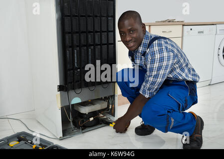 Junge Glücklich afrikanische Techniker in einheitliche Festsetzung Kühlschrank in der Küche Zimmer Stockfoto