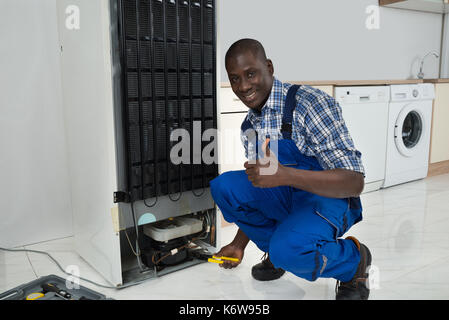Junge Glücklich afrikanische Techniker in einheitliche Festsetzung Kühlschrank in der Küche Zimmer Stockfoto