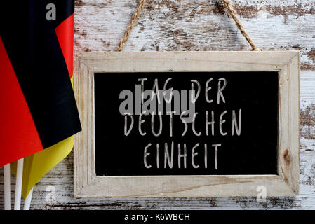 Nahaufnahme der eine Tafel mit dem Text Tag der Deutschen Einheit Tag der Deutschen Einheit in Deutsch geschrieben, und einige Fahnen von Deutschland gegen eine rustikale Woo Stockfoto