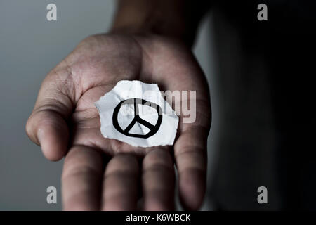 Nahaufnahme eines jungen Mannes mit einem Blatt Papier mit einem Friedenssymbol in ihm, in seine Handfläche gezeichnet Stockfoto