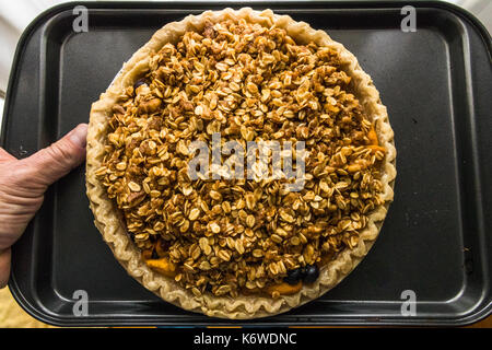 Horizontale Foto einer Blaubeere und Pfirsich Kuchen mit ein haferflocken Topping auf einem rechteckigen grauen Fach gehalten wird Stockfoto