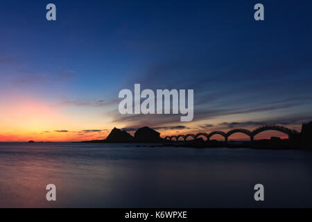 Eine kleine Insel vor der Küste und die berühmte achtbogenförmige Fußgängerbrücke, die vor dem Dämmernachthimmel steht, in Sanxiantai in Taitung, Taiwan Stockfoto