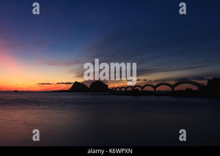 Eine kleine Insel vor der Küste und die berühmte achtbogenförmige Fußgängerbrücke, die vor dem Dämmernachthimmel steht, in Sanxiantai in Taitung, Taiwan Stockfoto