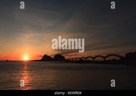 Eine kleine Insel vor der Küste und die berühmte Fußgängerbrücke mit acht Bögen, die bei Sonnenaufgang in Sanxiantai in Taitung, Taiwan, umrissen wurde Stockfoto