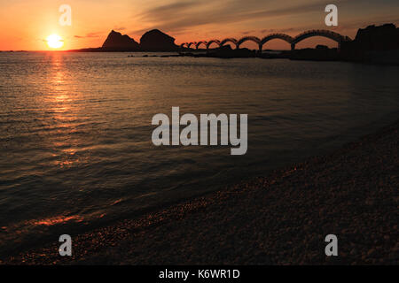 Eine kleine Insel vor der Küste und die berühmte Fußgängerbrücke mit acht Bögen, die bei Sonnenaufgang in Sanxiantai in Taitung, Taiwan, umrissen wurde Stockfoto