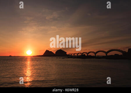 Eine kleine Insel vor der Küste und die berühmte Fußgängerbrücke mit acht Bögen, die bei Sonnenaufgang in Sanxiantai in Taitung, Taiwan, umrissen wurde Stockfoto