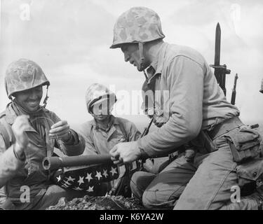 Drei Marines des 28 Regiment der 5th Marine Division durchgeführt die amerikanische Flagge auf dem Gipfel des Mount Suribachi auf Iwo Jima und während der Schlacht noch auf über andere Teile der Blutbefleckte Insel wütete, sie trotzig aufgeworfenen alten Ruhm in den Gesichtern der Feind. Iwo Jima, 23. Februar 1945. Foto von Lou Lowery. Stockfoto