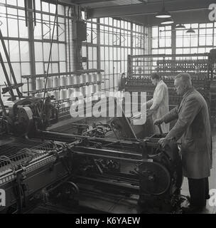 1950, historische, Bild zeigt Männer in Latzhosen arbeitenden großen komplexen mechanischen Maschinen, ein Spinner und Spinning Mule in der kammgarn Spinningraum, Leeds, England, UK. Kammgarn ist eine feine glatte Stoff aus langen Fasern der Wolle Garn und der spining Prozess langsamer ist. Stockfoto
