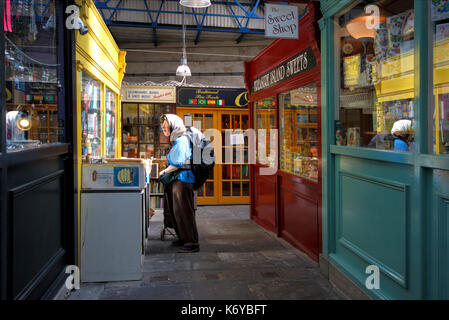 Eine ältere Frau durchsuchen Second Hand Bücher auf einem Tisch außerhalb eines second hand Book Shop. Es ist eine Markthalle, in Bristol, Großbritannien Stockfoto