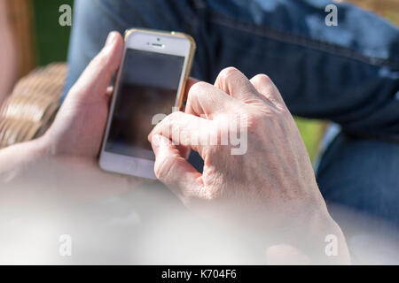 Senior, reifer Mann mit mobilen Smart Phone im Freien im Garten entspannen Sie sich im Sommer Sonne in Großbritannien Stockfoto