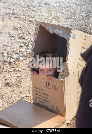 Ein Kind spielt gerne, versteckt in einem Karton auf den kargen steinigen Boden des Ritsona Flüchtlingslager in Griechenland. Stockfoto