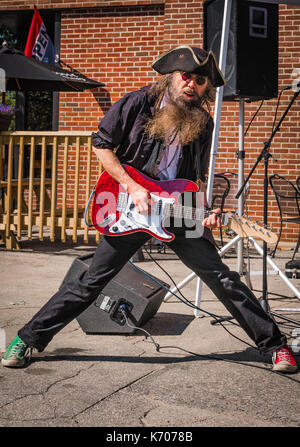 Ein Kaukasier Männlich rock guitar Interpret in einem schwarzen Hemd und Piraten Hut singt in einem lokalen outdoor Music Festival in Keene, NH. Stockfoto