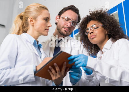 Gruppe der Wissenschaftlichen Mitarbeiter Notizen die Forschung im Labor, Mix Race Team der Wissenschaftler die Ergebnisse des Experimentes oder Diagnose In Tabl Stockfoto
