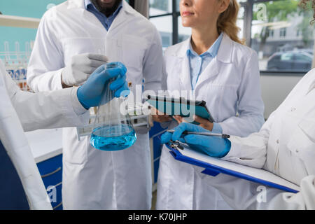 Wissenschaftler Hand, die Kolben und die Gruppe der Forscher machen Sie sich Notizen von Forschung im Labor, in der wissenschaftliche Mitarbeiter Analyse Experiment im Labor Stockfoto