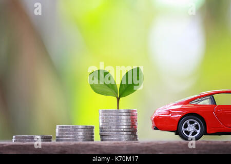 Grüne Keimlinge Baum wachsen auf Münzen von Graph und rotes Auto im Konzept der Investition und Speichern ein Fahrzeug zu kaufen. Stockfoto