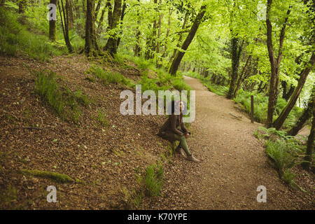 Die ganze Länge der Frau sitzt durch Schmutz Straße am Wald Stockfoto