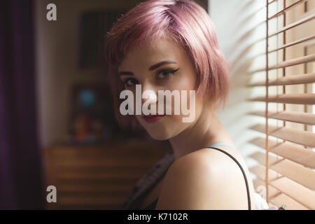 Porträt der jungen Frau mit gefärbten Haaren durch die Fenster zu Hause Stockfoto