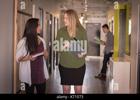 Weibliche Kollegen diskutieren im Korridor im Büro Stockfoto