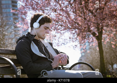 Man Musik hören während sitzt auf der Bank im Park Stockfoto