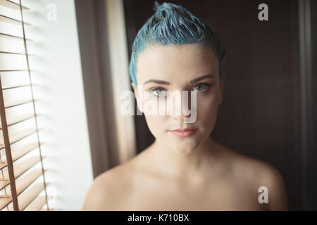 Porträt der jungen Frau mit gefärbten Haaren durch die Jalousien zu Hause Stockfoto