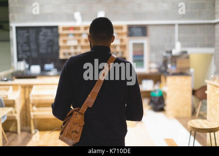 Ansicht der Rückseite des jungen Mannes mit Tasche im Cafe Stockfoto