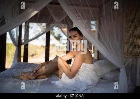 Portrait der Frau in Handtuch sitzen auf einem Himmelbett im Cottage Stockfoto