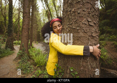 Junge Frau mit geschlossenen Augen umarmt Baum im Wald Stockfoto
