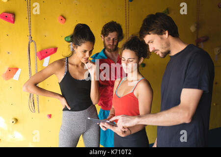 Freunde mit digitalen tablet, während durch die Kletterwand in der Turnhalle stehen Stockfoto