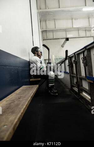 Männliche Eishockeyspieler mit Mannschaftskameraden entspannen auf Sitz am Gang Stockfoto
