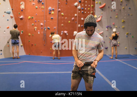 Mann binden Sicherheit während der Athleten Kletterwand im Hintergrund bei gym Stockfoto