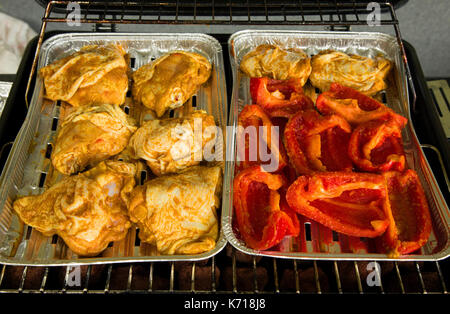 Hähnchenschenkel in Gewürzen und Stücke von Paprika auf den Tabletts auf dem Grill braten. Schließen, horizontale Ansicht. Stockfoto