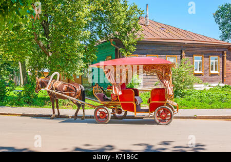 Die Beförderung mit Pferd wartet auf die Touristen neben der Susdaler Kreml, den traditionellen Log House ist auf Hintergrund gesehen, Russland. Stockfoto