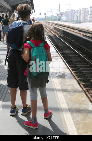 Junge Bruder und kleine Schwester mit Rucksäcken warten auf den Zug Stockfoto