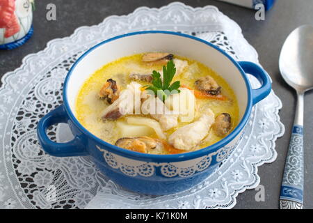 Cremige Suppe mit Fischfilet und Muscheln in einem blauen Keramik Topf auf einem weißen Tuch an einem grauen Abstrakt Hintergrund. Gesunde Ernährung Konzept. Meditteranian Lebensstil. Stockfoto