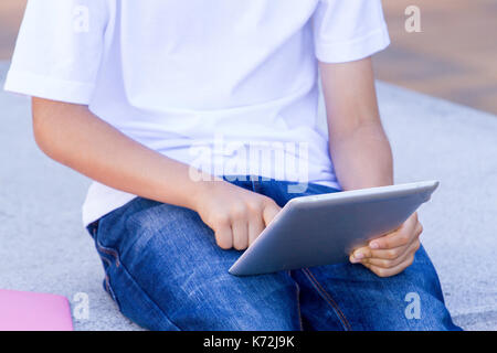 Die Hand des Kindes mit Tablet Computer und Bücher. Nahaufnahme Stockfoto