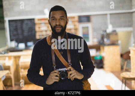 Porträt der jungen Mann mit Kamera, während im Cafe stehend Stockfoto