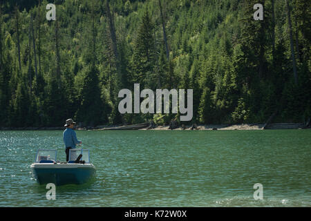 Seitenansicht der Mann angeln beim Stehen auf dem Boot in Fluss gegen Baum Stockfoto