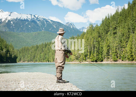Die ganze Länge der Mann angeln im Fluss beim Stehen auf Ufer gegen Berg Stockfoto