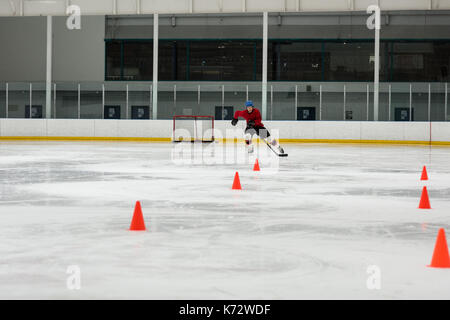 Männliche Eishockey Spieler üben Bohrer durch sport training Kegel an der Eisbahn Stockfoto