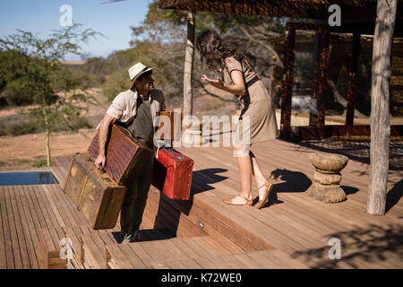 Frau gestikuliert während der Mann, der einen Koffer während der Safari Ferienhäuser Stockfoto