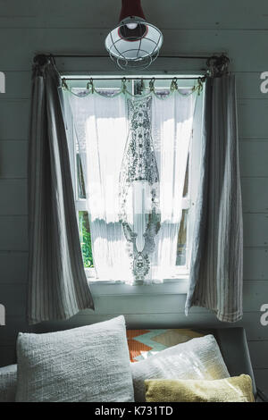 Sofa mit weiß und beige Kissen vor Fenster mit Fensterläden. Innenraum der rustikalen Holzhaus mit weißen Wänden, Sonnenlicht in Fenster Stockfoto