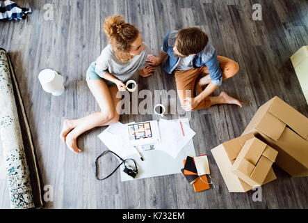 Junges Ehepaar Umzug in neues Haus, sitzen auf dem Boden in der Nähe von Kartons, trinken Kaffee. Stockfoto