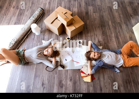 Junges Ehepaar Umzug in neues Haus, auf dem Boden liegend in der Nähe von Kartons, trinken Kaffee. Stockfoto