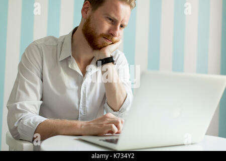 Porträt der jungen Haar Mann bei der Arbeit am Laptop im Zimmer durch den blauen Streifen an der Wand Stockfoto