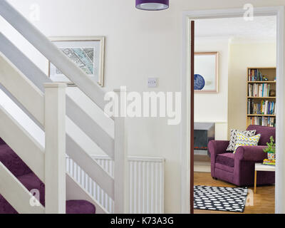 Die Treppe in einer typischen uk home Eingangsbereich mit Blick in ein Wohnzimmer, eine komfortable violett Stuhl und andere Möbel Stockfoto