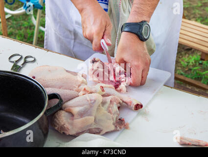 Der Mann mit Messer schneiden und Schnitzen rohes Huhn auf weißer Tisch. Vorbereitung der Zutaten für die Paella Jambalaya, Grill im Freien, Picknick, Weeke Stockfoto